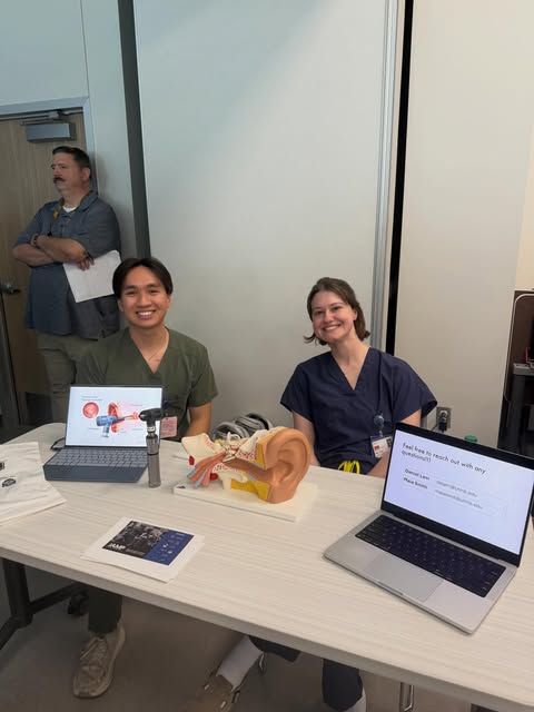 Students in scrubs at an educational table with ear and head anatomy models