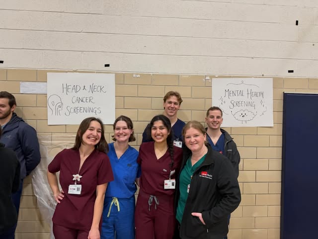 A group in scrubs beside head and neck cancer screening posters